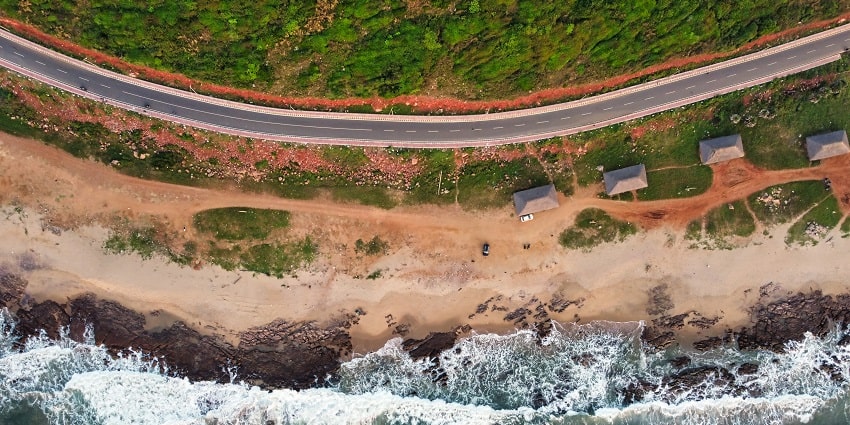 An aerial picture of a beach with a road moving parallel to it forming a flag like appearance