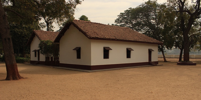 A cottage surrounded by trees on a sandy surface