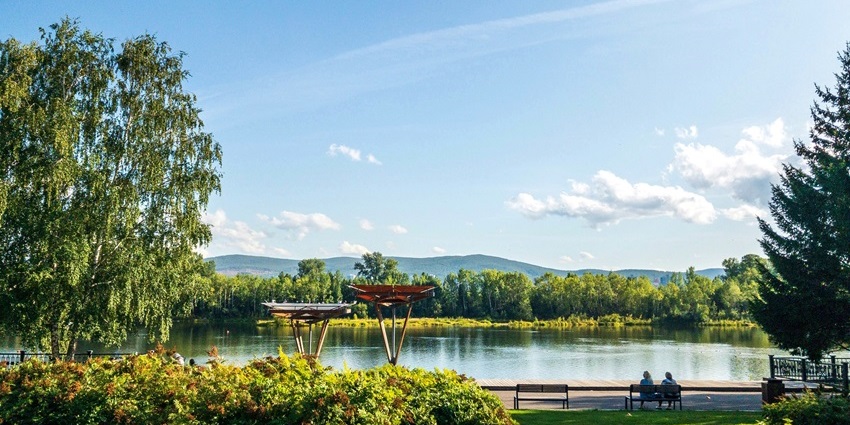 Brown wooden bench on green grass near the lake at Sadhankeri Park during the daytime.