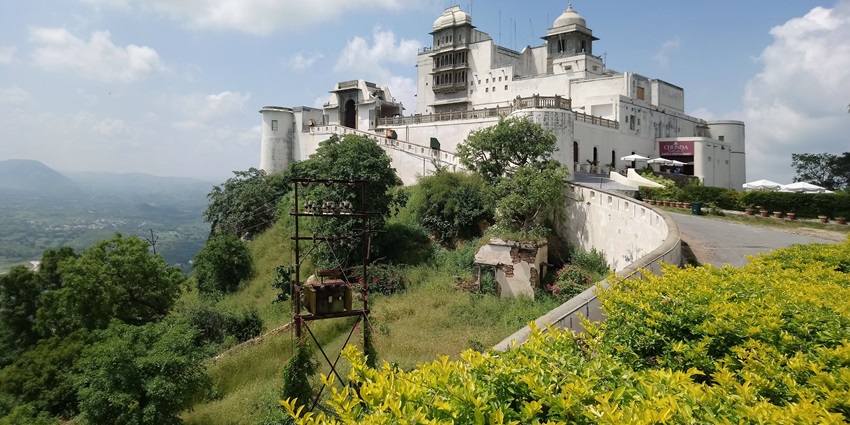A panoramic view of the Sajjangarh Monsoon Palace surrounded by green vegetation.