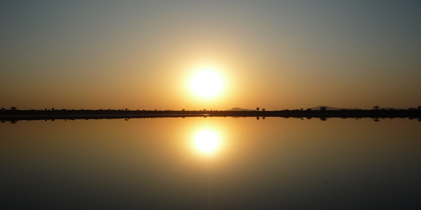 A serene sunset over Sambhar Lake with calm waters reflecting the vibrant colours of the sky.