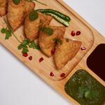 A glimpse of hot samosas being served on a plate with red and green chilli chutney.