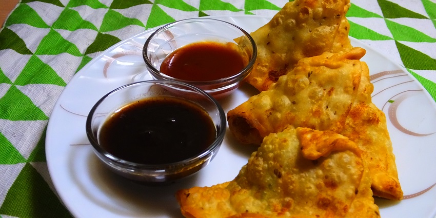 An image of crispy samosas with spiced potatoes and peas, served with chutneys.