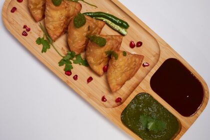 A glimpse of hot samosas being served on a plate with red and green chilli chutney.