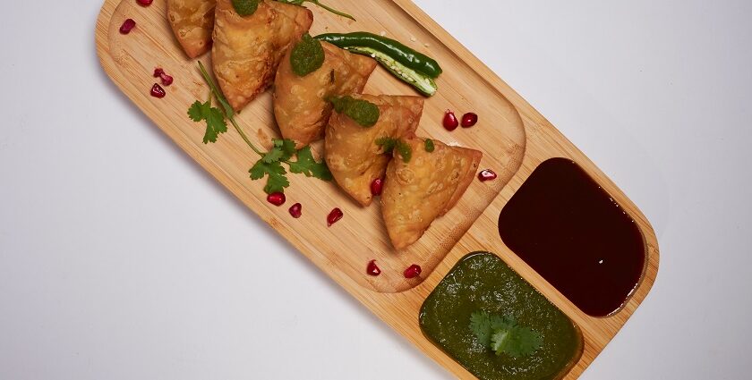 A glimpse of hot samosas being served on a plate with red and green chilli chutney.