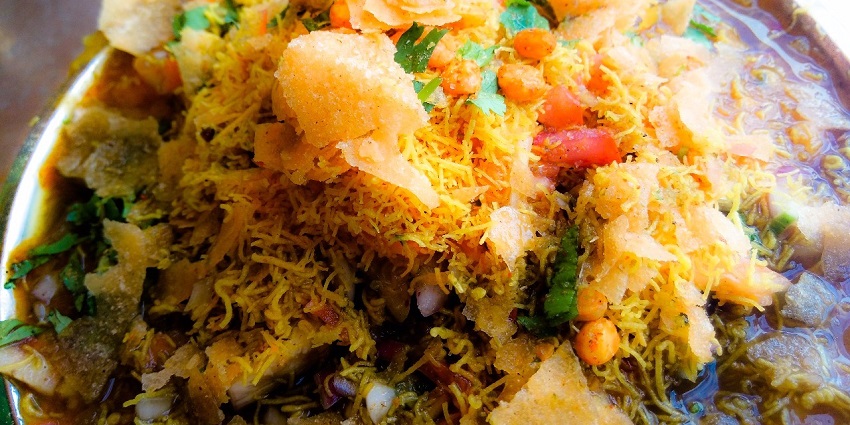 Samosas topped with yoghurt, tamarind chutney, and spices, served as a flavorful snack.