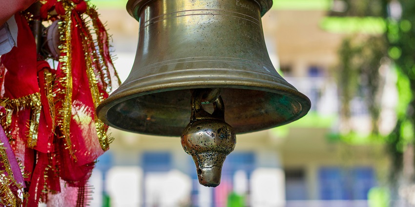 A close-up of a beautifully crafted golden temple bell with a red piece of cloth on it.