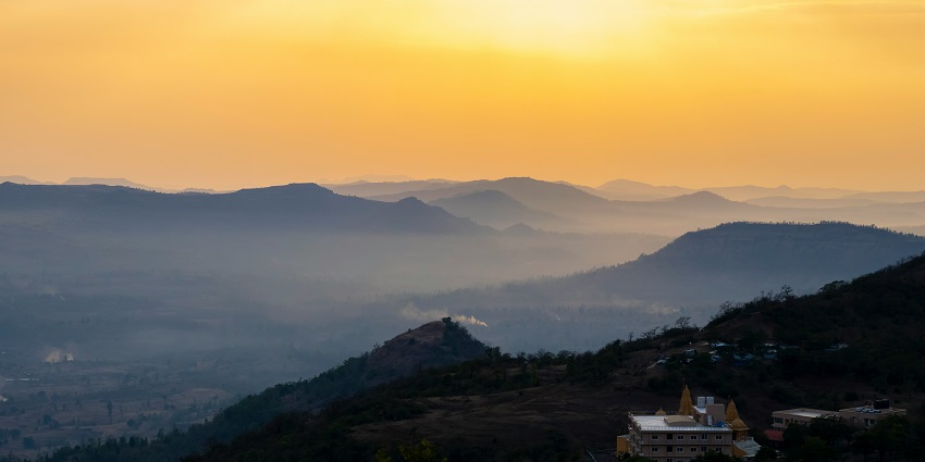 A breathtaking view of Saputara city with lush green hills and houses during the sunset.