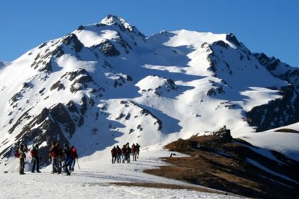 Trekkers crossing snow-covered terrain at the Sar Pass trekking in the Himalayas, surrounded by peaks