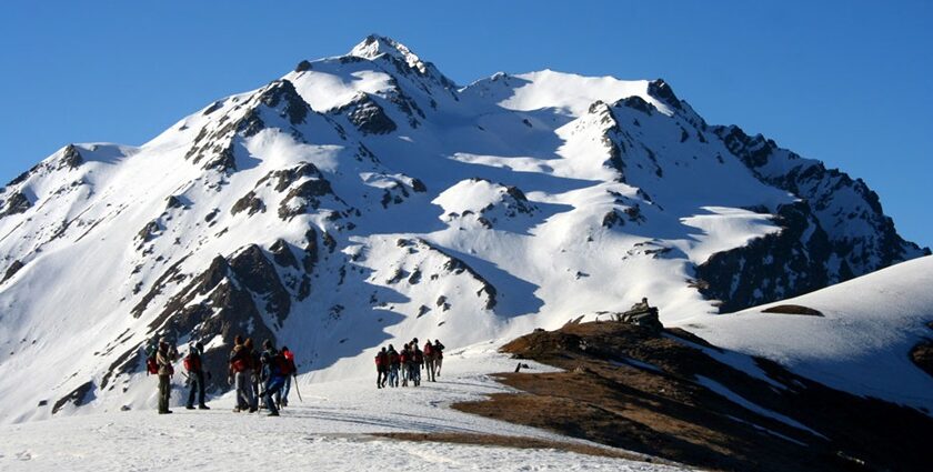 Trekkers crossing snow-covered terrain at the Sar Pass trekking in the Himalayas, surrounded by peaks