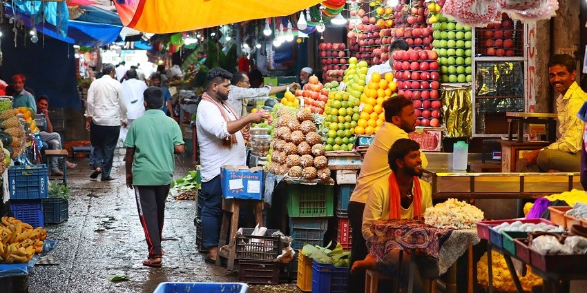 A vibrant Indian bazaar with men selling a variety of fresh fruits in colourful market stalls, a popular place near Indore Zoo.