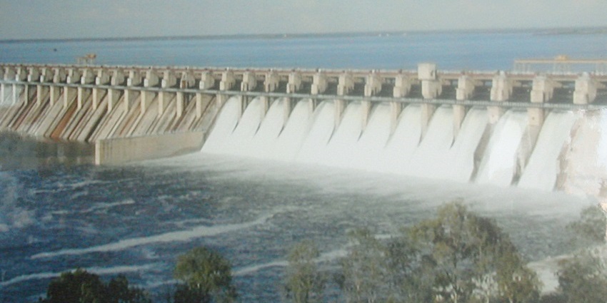 Upstream view of a dam with calm reservoir and surrounding green hills.