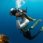 A mesmerising view of a school of orange fish swimming underwater with a scuba diver.