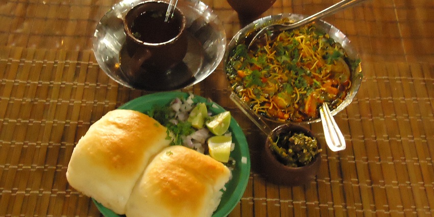 Sev Usal is a spicy dish served with a pav and garnished with onions and a slice of lemon.