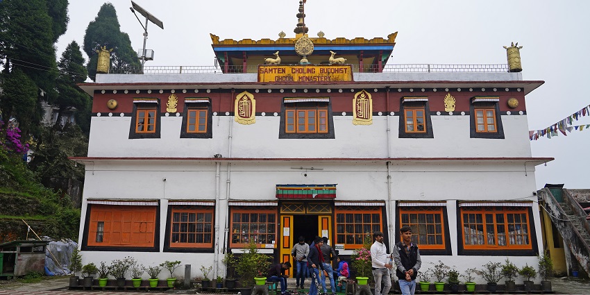 View of Sherab Ling Monastery, with its vibrant red and gold walls, surrounded by the lush greener