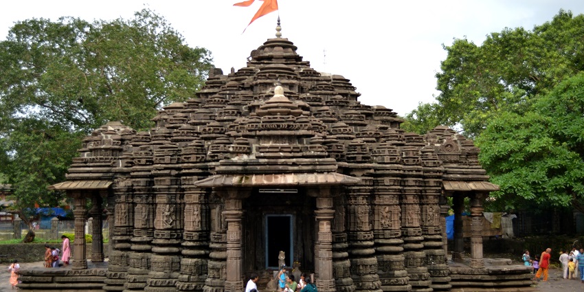 A picture of a Shiva temple built in the traditional architecture and intricate designs with a flag on top