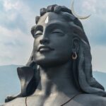 A picture of a majestic statue of Lord Shiva with tourists visiting the attraction and a hill station in the background