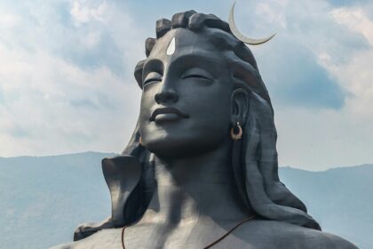 A picture of a majestic statue of Lord Shiva with tourists visiting the attraction and a hill station in the background