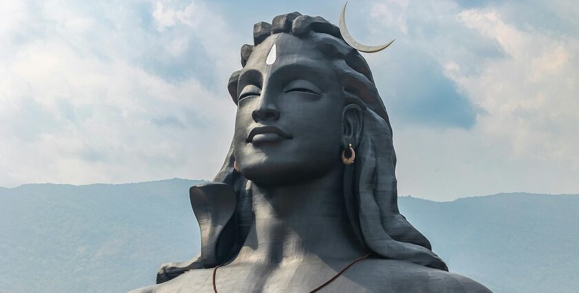 A picture of a majestic statue of Lord Shiva with tourists visiting the attraction and a hill station in the background