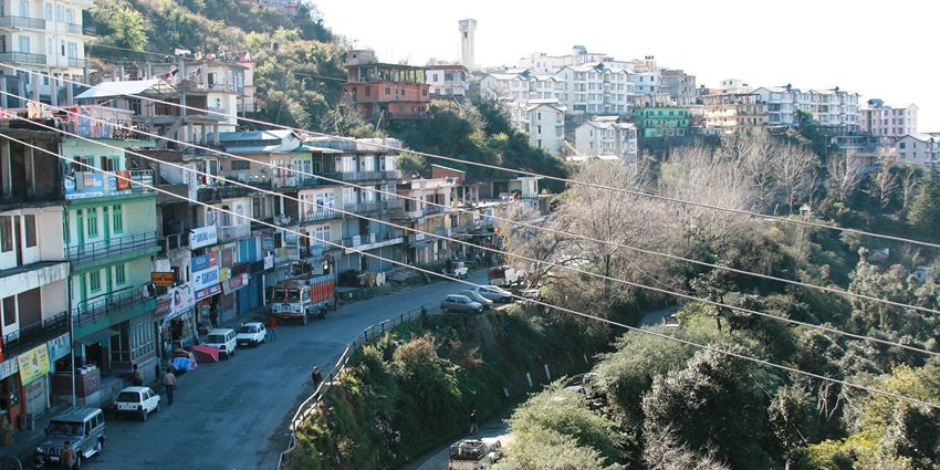 A picture of a hillside town in Himachal Pradesh with curving roads and lush mountains