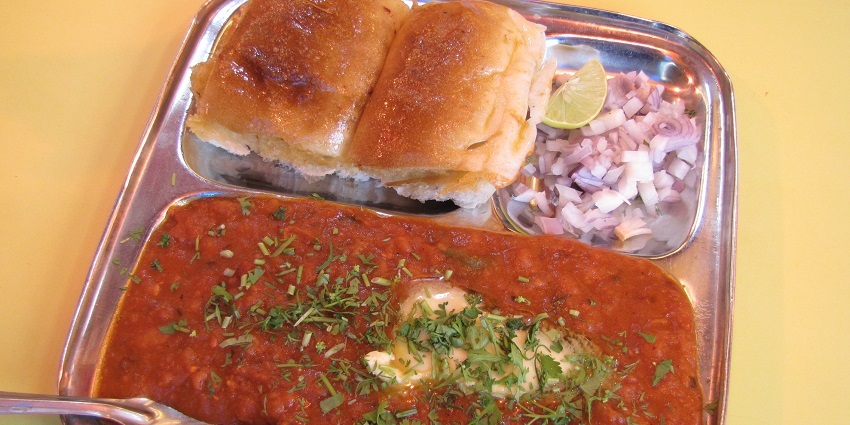 Spicy pav bhaji served with bread rolls and garnished with onions and lemon