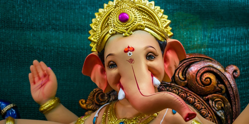 A picture of an Idol of lord Ganesh with a golden crown and a beautiful blue background.