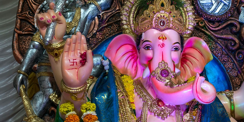 A picture of an idol of Lord Ganesha made out of stone with a woman praying in front of it