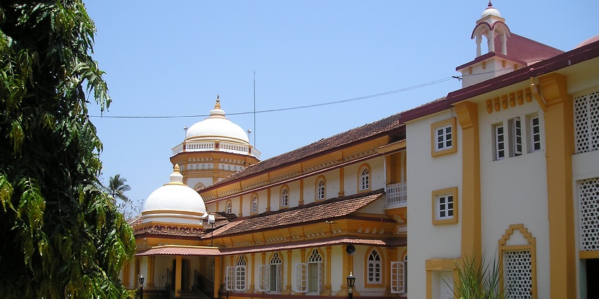 Image of Shri Ramnath Temple with yellow and white architecture, surrounded by lush green trees