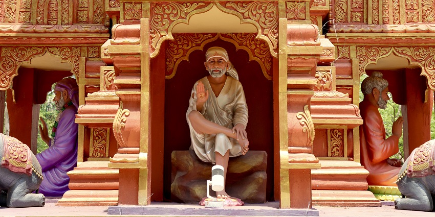 A statue of Sri Sai Baba dressed in traditional white robes and a headscarf.