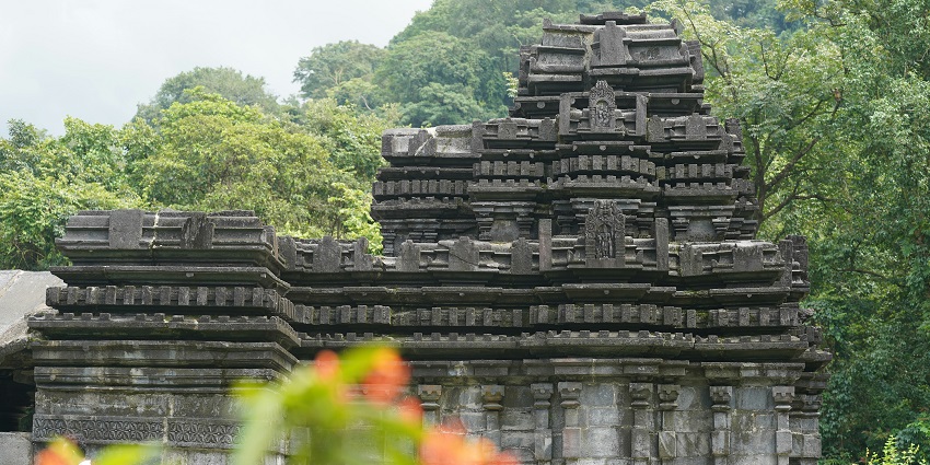 A view of the Shri Shantadurga Temple made of grey stones surrounded by greenery.