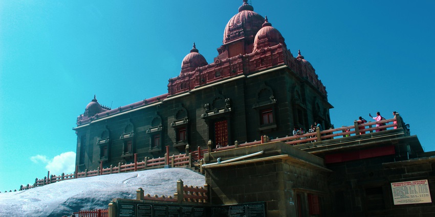 Large classical building of a temple with arches and columns beside a canal under a blue sky.