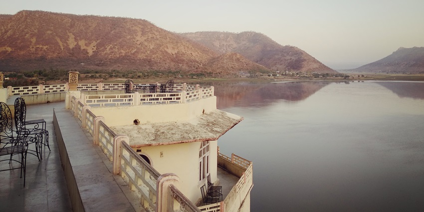 A photo of Siliserh Lake surrounded by a historic palace with a misty background