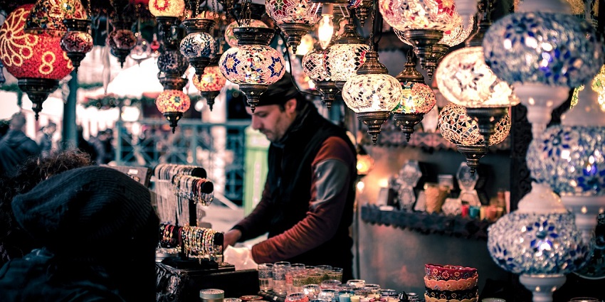 Market booth displaying various items, including bracelets, candles, and colourful textiles.
