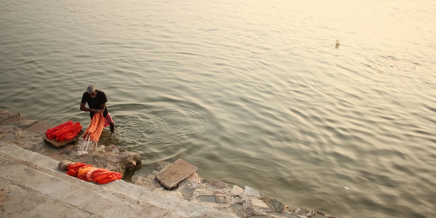 Photo of the person putting small diyas while the water mimics the lights produced by it.