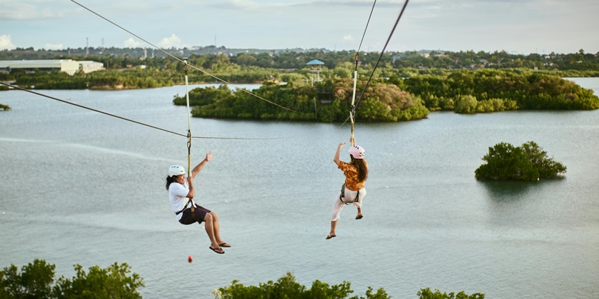 People soaring on a zip line, over a calm lake for a high-adrenaline experience.