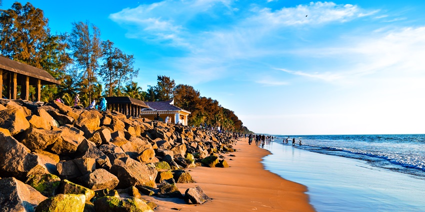A vibrant Snehatheeram Beach with golden sand, blue water and rocky formations.