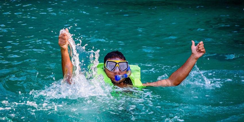 A man in the ocean, wearing snorkelling gear and showing a thumbs up sign with hands.