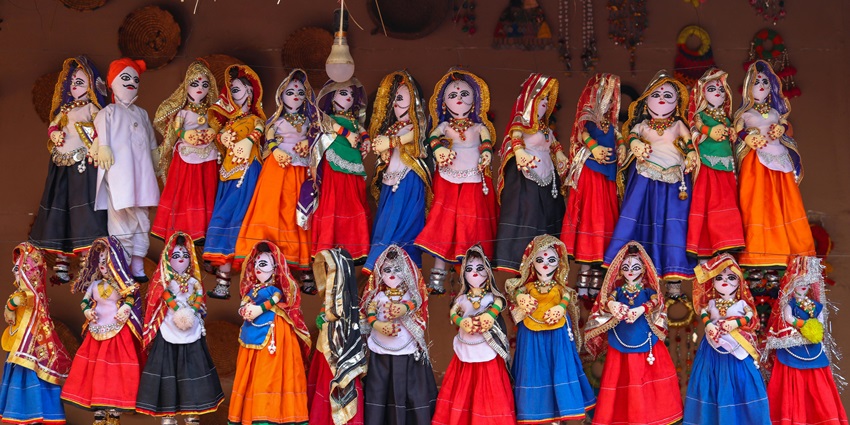 A vibrant display of colourful dolls hanging in rows against a textured wall at the beautiful Sojati Gate Museum.