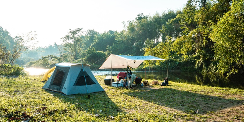 A tent in a lush, green forest surrounded by tall trees and soft sunlight filtering through.