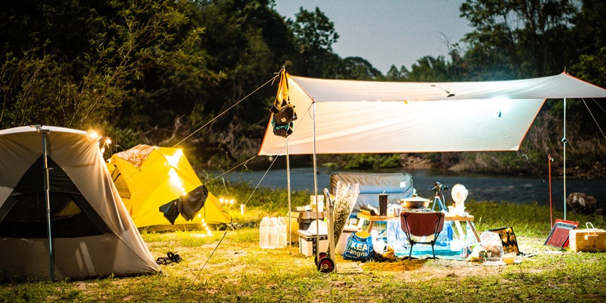 A glowing tent beside a campfire in a forest, illuminated under a starry night sky.