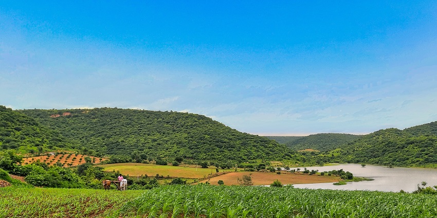 A picture of a field with a few hills in the background and a farmer ploughing the field