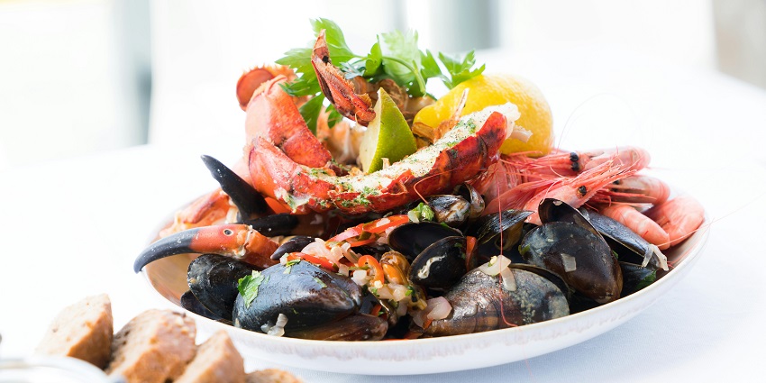 A tempting view of a ceramic plate served with seafood with a wedge of lemon on it.