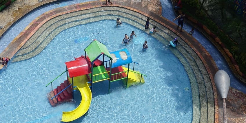 A picture of fun slides in the centre of a swimming pool with kids playing around it.