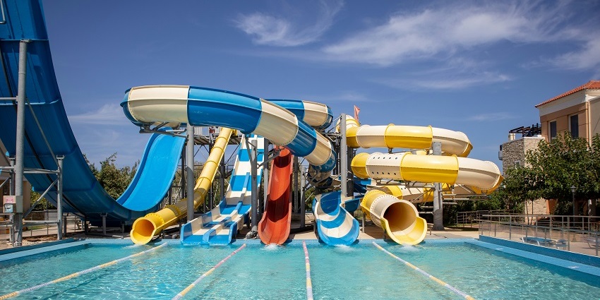 A picture of multicoloured slides over a swimming pool and cloudy sky in the background.