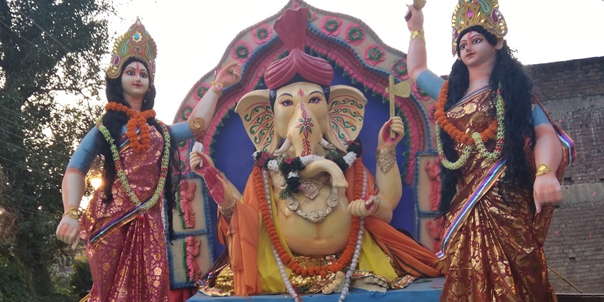 A picture of an idol of lord Ganesha along with statues of two devotees praying in front of him