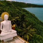 A breathtaking view of a large statue of Buddha surrounded by lush greenery and an ocean.