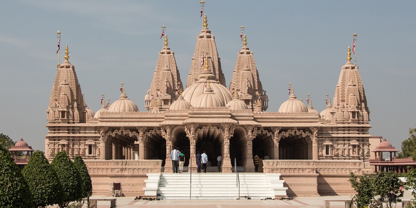 A picture of a majestic temple built using traditional Hindu architecture, surrounded by lush gardens
