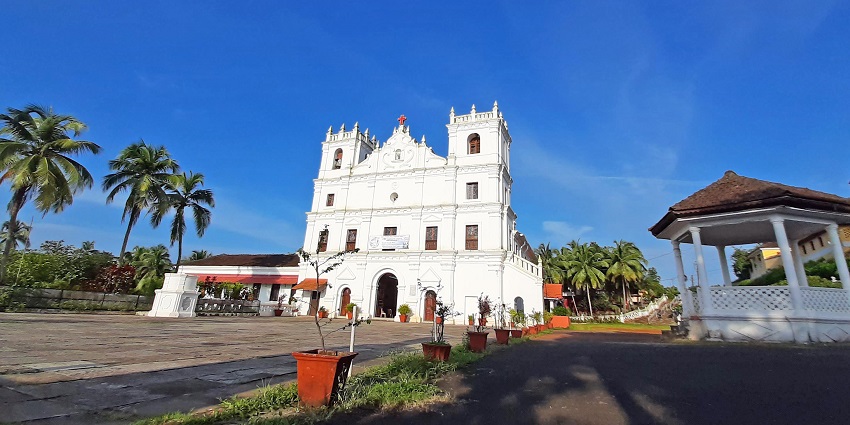 Panoramic view of the white church against the blue sky and tall palms standing nearby