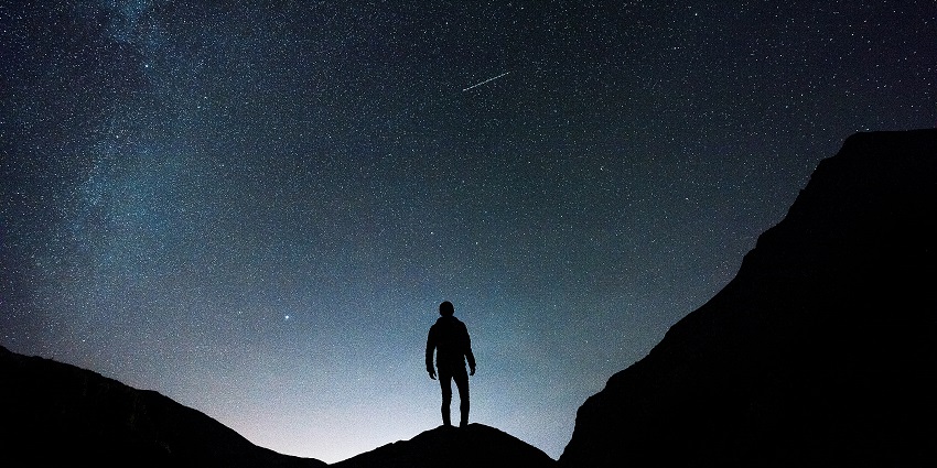 A breathtaking vista of a person standing under the canopy of stars and watching the sky.