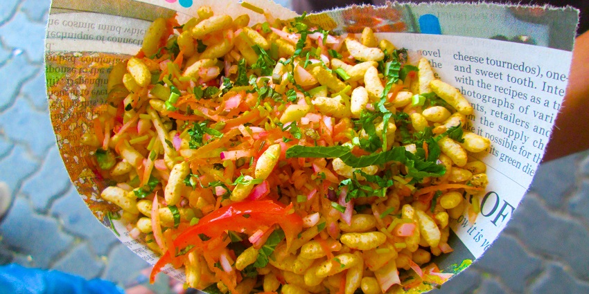 A colorful plate of bhel puri topped with onions, tomatoes, and chutneys served.